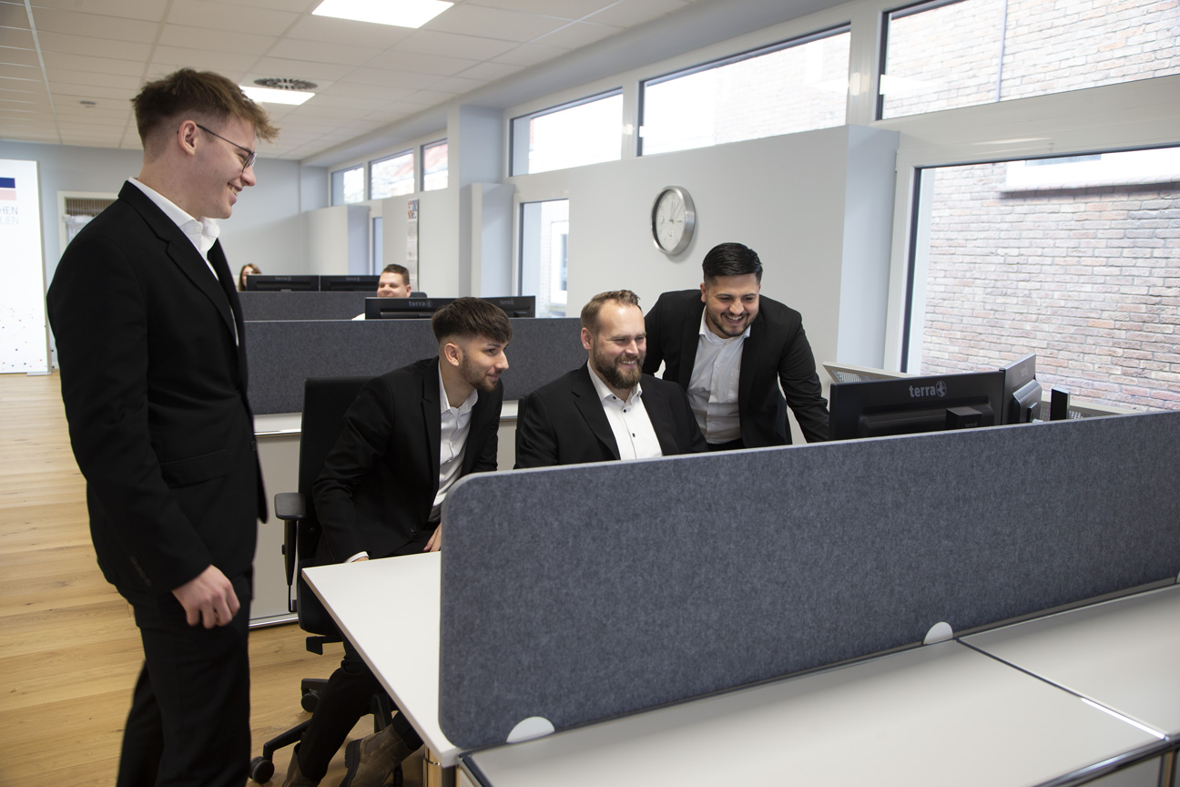 Zwei Immobilienmakler von Claashen Immobilien und zwei Auszubildene zum Immobilienkaufmann sitzen um einen PC herum